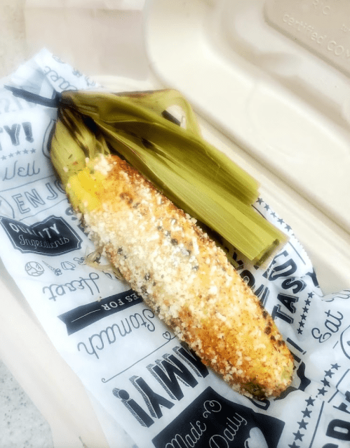Grilled corn on the cob topped with cheese and spices, served in a paper wrapper.