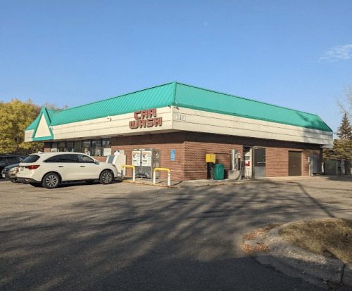 A car wash building with a teal roof and brick exterior, featuring a few cars parked outside on a sunny day.