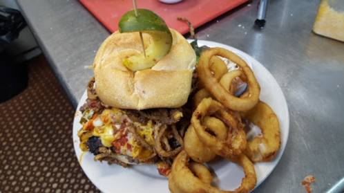 A hearty burger topped with cheese and jalapeños, served with crispy onion rings on a white plate.