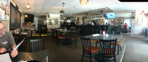 A panoramic view of a casual restaurant interior with empty tables, a bar area, and a few patrons.