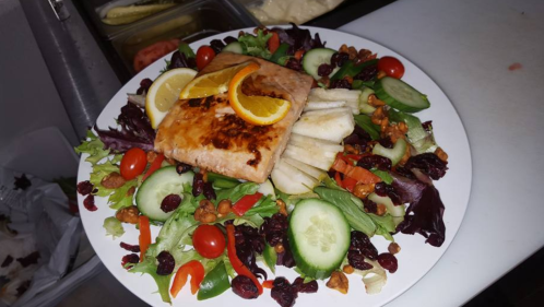 A colorful salad topped with grilled salmon, lemon slices, cucumbers, cherry tomatoes, and mixed greens.
