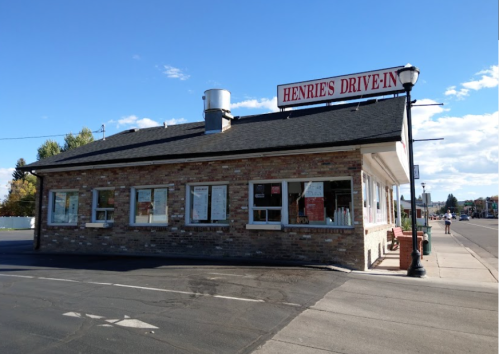 A brick building with a sign reading "Henrie's Drive-In," featuring large windows and a clear blue sky.