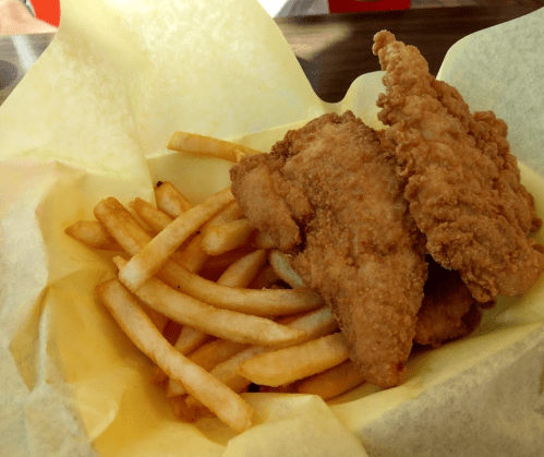 A basket of golden French fries topped with two crispy fried chicken tenders.