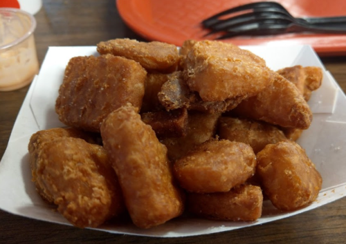 A pile of golden-brown, crispy chicken nuggets served in a white paper tray.