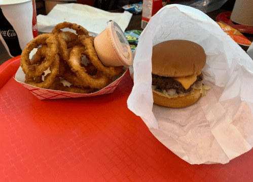A tray with a burger wrapped in paper and a side of onion rings with dipping sauce.