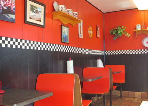 A retro diner interior with red walls, checkered accents, and red booths, featuring vintage decor and a cozy atmosphere.