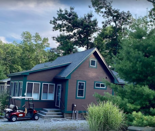 A charming brown house with green trim, surrounded by trees, featuring a golf cart parked in front.