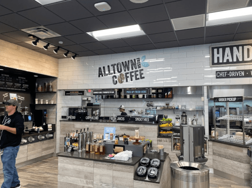 Interior of a modern coffee shop with a menu board, coffee machines, and a variety of beverages displayed.