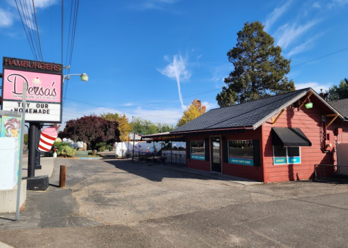 A red hamburger restaurant with a sign, surrounded by trees and a clear blue sky.