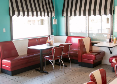 A retro diner interior featuring red and white booths, tables, and striped awning windows.