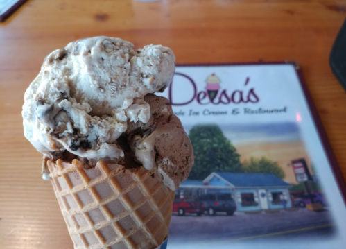 A close-up of a waffle cone filled with chocolate and vanilla ice cream, with a menu in the background.