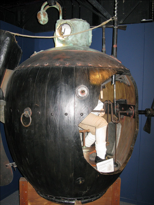 A vintage submarine model with a round, black exterior and a visible interior, showcasing a seated figure inside.