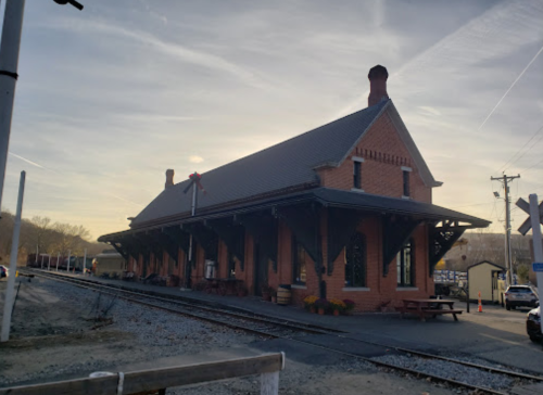 Historic brick train station at sunset, with tracks and a clear sky in the background.