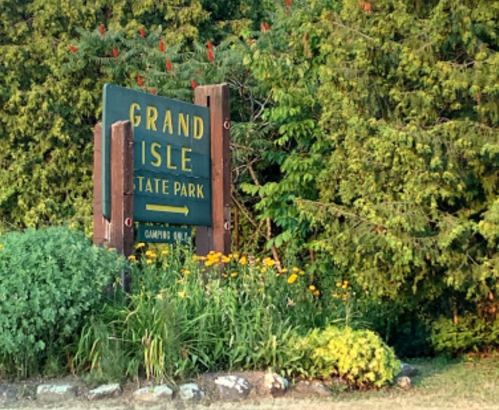 Sign for Grand Isle State Park surrounded by greenery and colorful flowers.