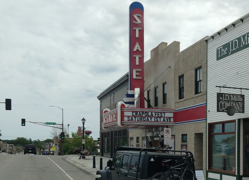 A vintage theater marquee reads "Crapola Fest" with a black vehicle parked nearby on a street.