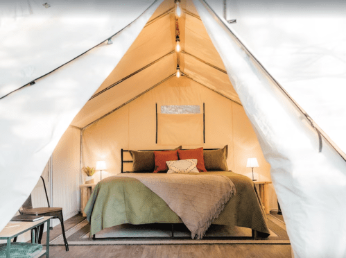 Cozy glamping tent interior with a bed, decorative pillows, and soft lighting.