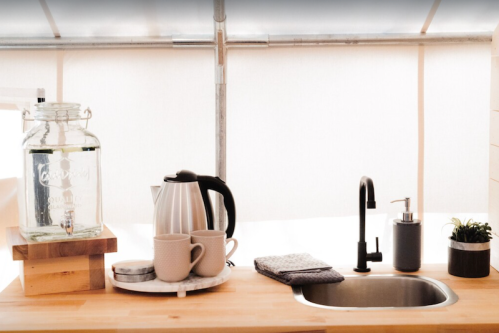 A cozy kitchen setup with a water dispenser, kettle, mugs, and a sink, all on a wooden countertop.