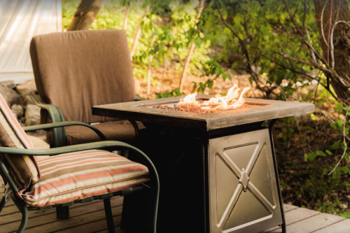 A cozy outdoor seating area with two chairs and a fire pit surrounded by greenery.