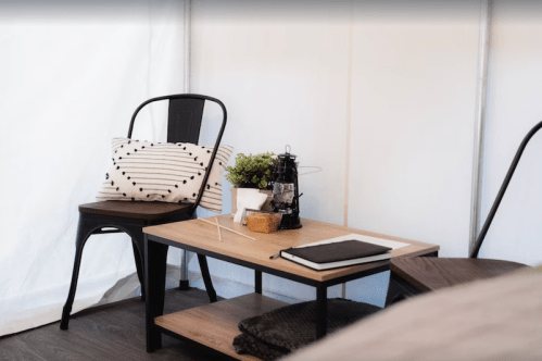 Cozy interior of a tent featuring a wooden table, chairs, a lantern, and decorative pillows.