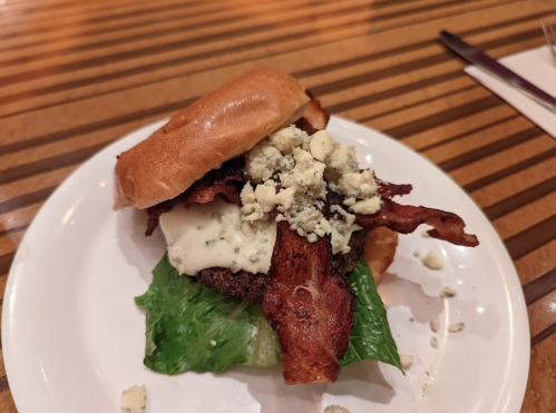 A burger with lettuce, bacon, and blue cheese on a toasted bun, served on a white plate.
