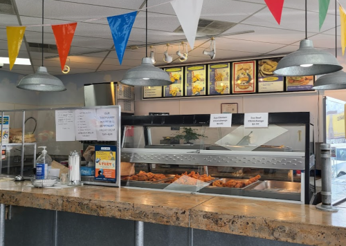 A counter in a fast-food restaurant with a display of fried food, menus above, and colorful bunting hanging from the ceiling.