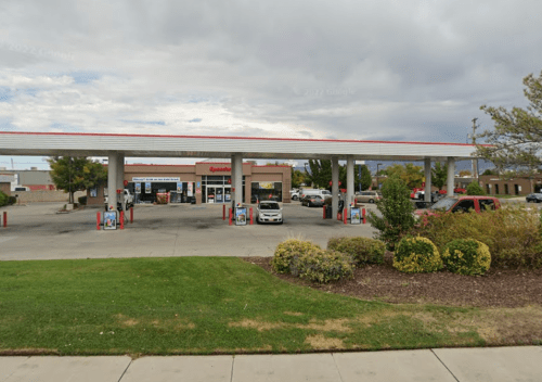 A gas station with multiple pumps, a convenience store, and parked cars under a cloudy sky.