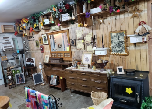 A cozy shop interior featuring wooden shelves, vintage decor, a mirror, and a rustic dresser against a wooden wall.