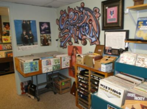 A cozy record store with vinyl records, posters on the walls, and a colorful graffiti mural.