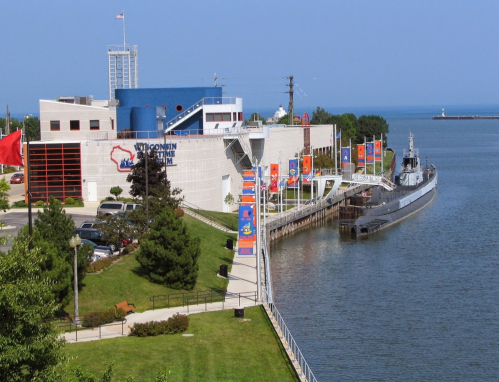 Exterior view of the Wisconsin Maritime Museum, featuring colorful banners and a docked submarine along the water.