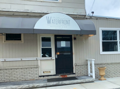 Exterior of "On the Waterfront" restaurant and bar, featuring a black door and a sign under a gray awning.