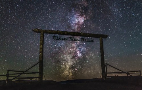 A starry night sky with the Milky Way above a wooden sign that reads "Eagle's Wing Ranch."