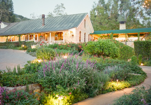 A charming stone house surrounded by lush gardens and soft evening lighting.