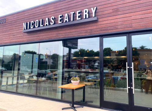 Exterior of Nicolas Eatery featuring large glass windows, a wooden facade, and a small table with a plant outside.