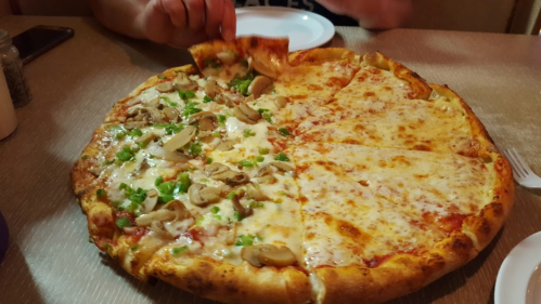 A large pizza divided in half: one side topped with cheese and the other with mushrooms and green peppers.