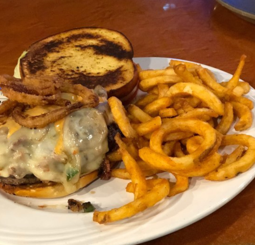 A plate with a cheeseburger topped with crispy onions and a side of curly fries.