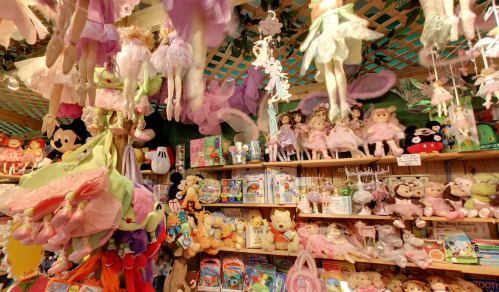 A colorful display of toys, including plush dolls, fairies, and stuffed animals, hanging and arranged on shelves.