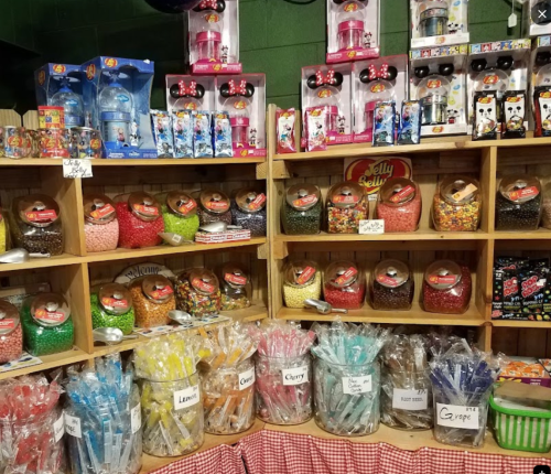 A colorful display of jars filled with various candies and toys on wooden shelves in a shop.