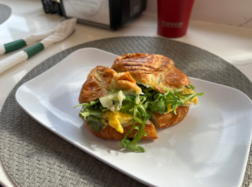 A flaky croissant sandwich filled with greens and scrambled eggs, served on a white plate.