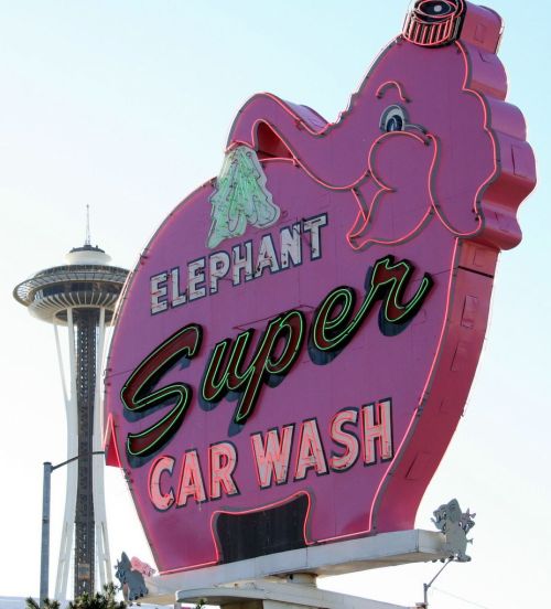 A large, pink elephant-shaped sign for "Elephant Super Car Wash" with the Space Needle in the background.