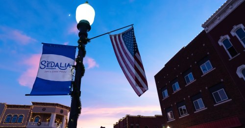 Looking up at a light pole with an American Flag and a Sedalia flag.