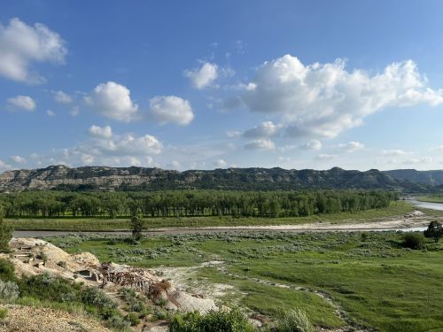 A scenic view of rolling hills, green trees, and a river under a partly cloudy sky.