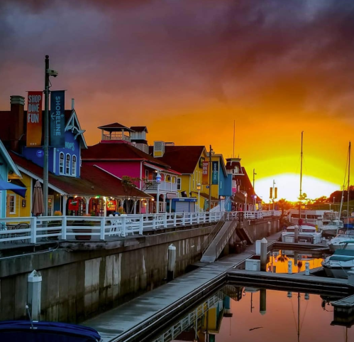 Colorful buildings line a waterfront at sunset, reflecting in calm waters with boats docked nearby.