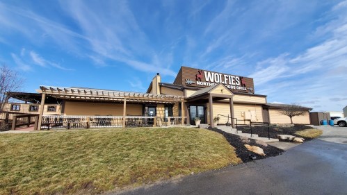 Exterior view of Wolfie's Northeast Food Grill, featuring a patio and signage against a blue sky.