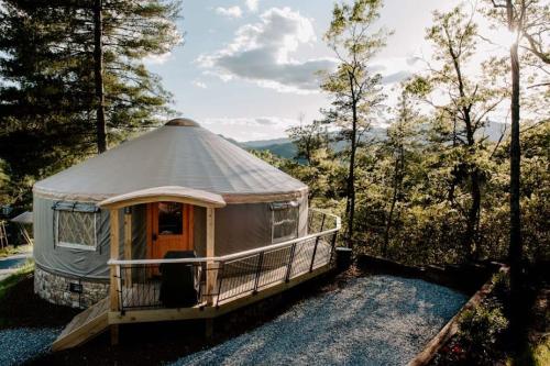 A cozy yurt surrounded by trees, with a wooden deck and scenic mountain views in the background.