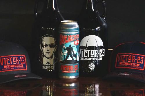 A display of craft beer items: a can, two growlers, and two hats, all featuring the Victor 23 logo and design.