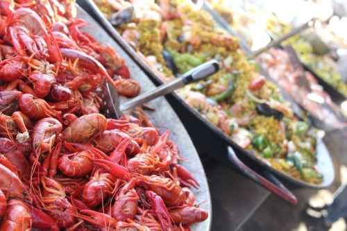 A close-up of a platter filled with vibrant red crawfish, alongside a colorful array of mixed seafood and rice dishes.