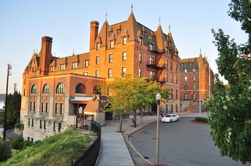 Historic brick building with a steeply pitched roof, surrounded by trees and a parking area, bathed in warm sunset light.