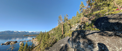 A scenic view of a lake surrounded by trees and rocky shores under a clear blue sky.