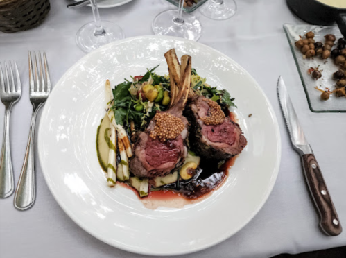 A gourmet plate featuring two lamb chops, greens, asparagus, and a rich sauce, elegantly presented on a white dish.