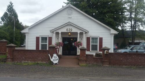 A charming white house with red shutters, featuring a "Tea Room" sign and flower arrangements at the entrance.